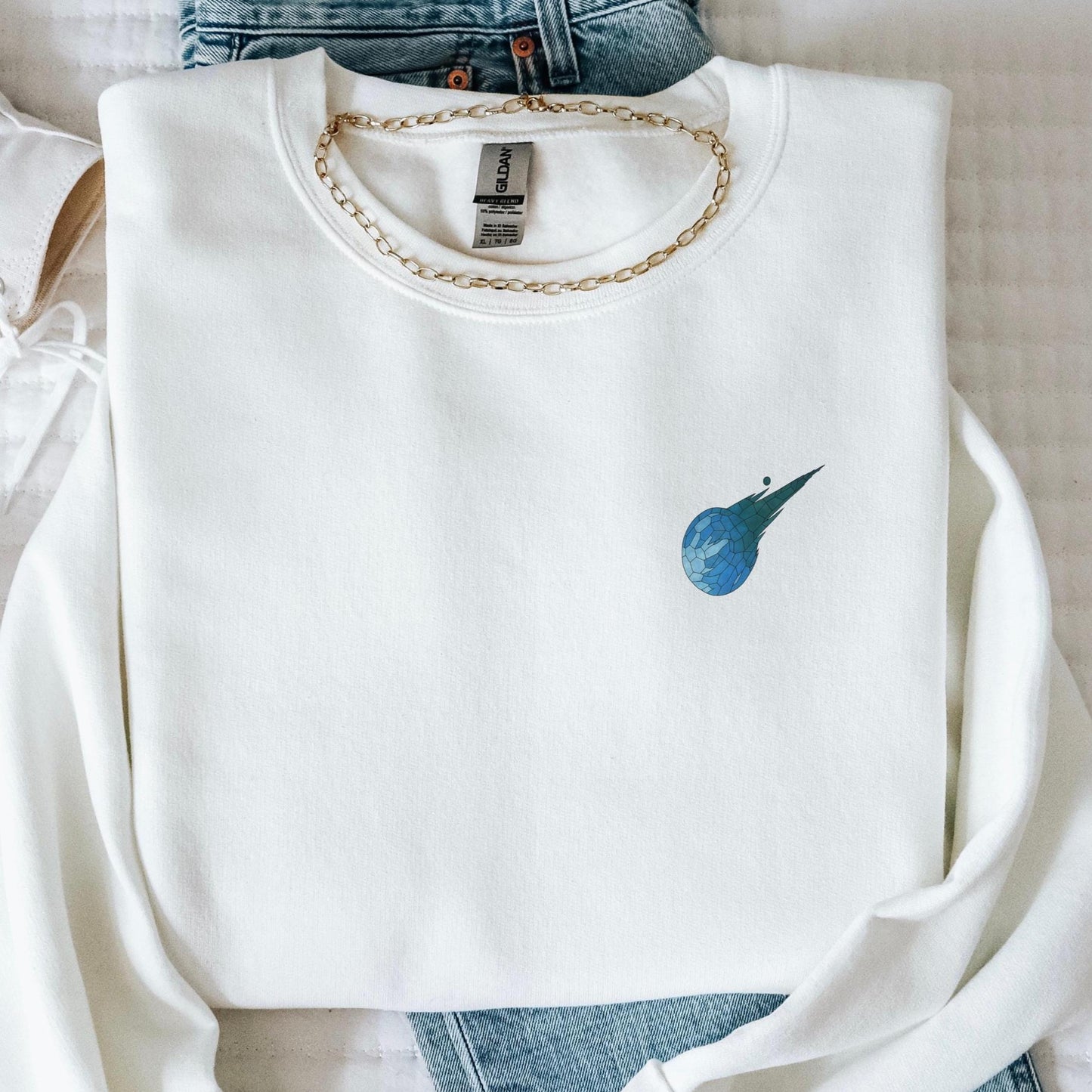 Stained glass style Final Fantasy meteor logo on a white sweater, folded lay.